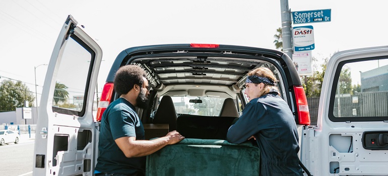a couple of movers packing a sofa in a moving van